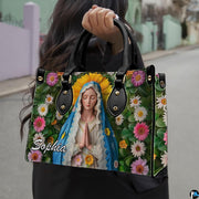Lifestyle presentation of the Virgin Mary botanical portrait handbag held outdoors