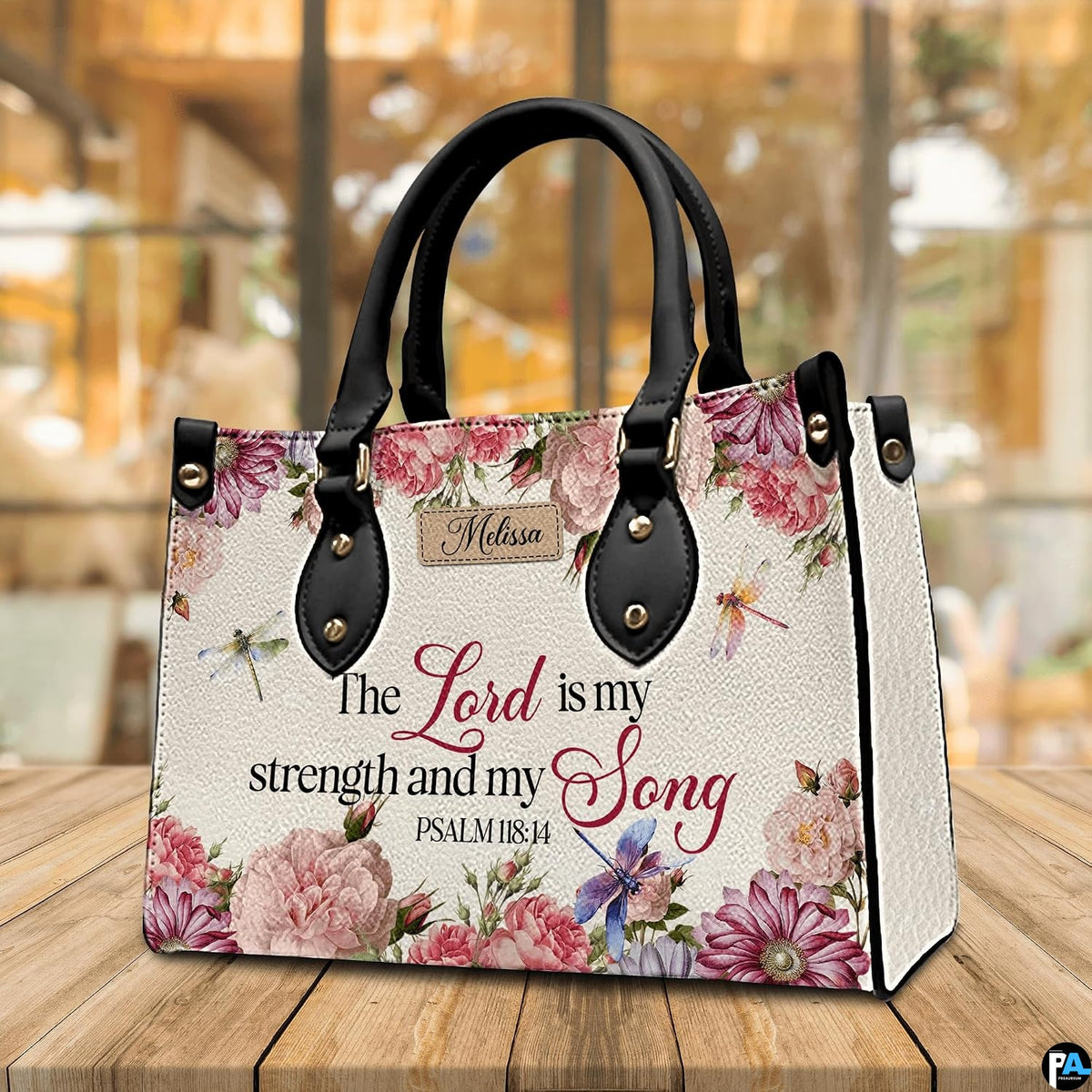 Scripture floral dragonfly handbag displayed on wooden tabletop in front of sunlit windows.