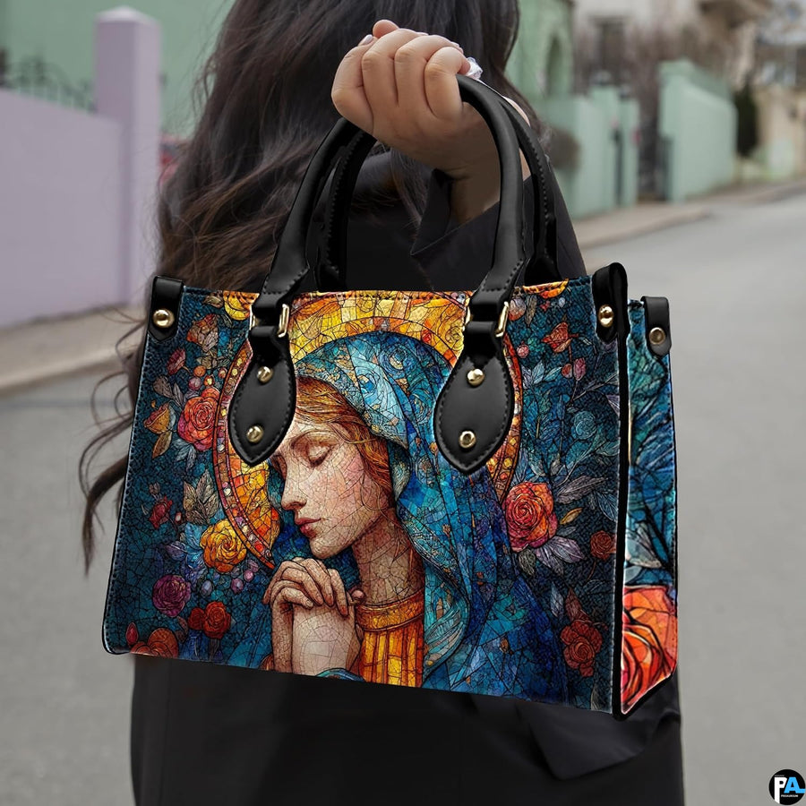 Handbag featuring praying Virgin Mary held outdoors by model in natural daylight.