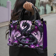 Gothic dragon handbag carried outdoors by top handles displaying the intricate black dragon and purple crystal artwork.