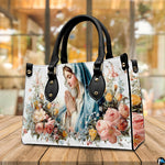 Front perspective of white handbag showing sky blue veil praying mary artwork surrounded by garden blossoms.