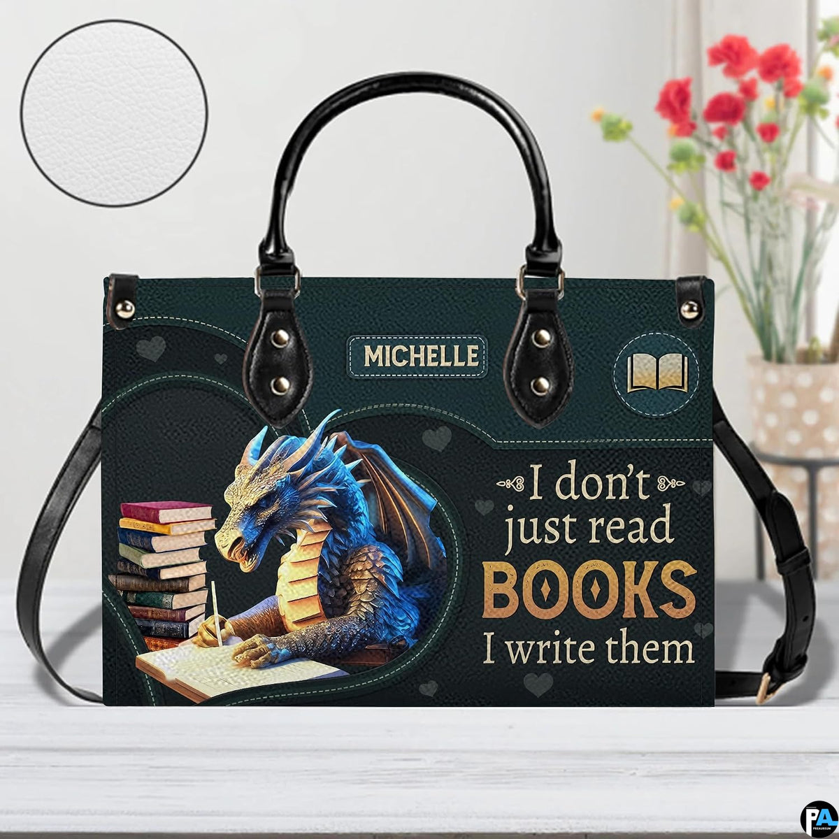 Author blue dragon handbag on white wooden table beside floral vase with texture swatch inset.