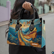Outdoor view showing model carrying African landscape gown accessory by top handle in natural daylight.