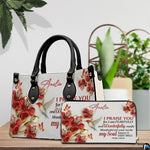 Hummingbird devotional handbag arranged with matching wallet on a tabletop beside decorative plant.
