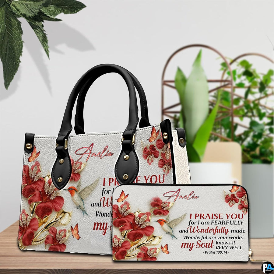 Hummingbird devotional handbag arranged with matching wallet on a tabletop beside decorative plant.