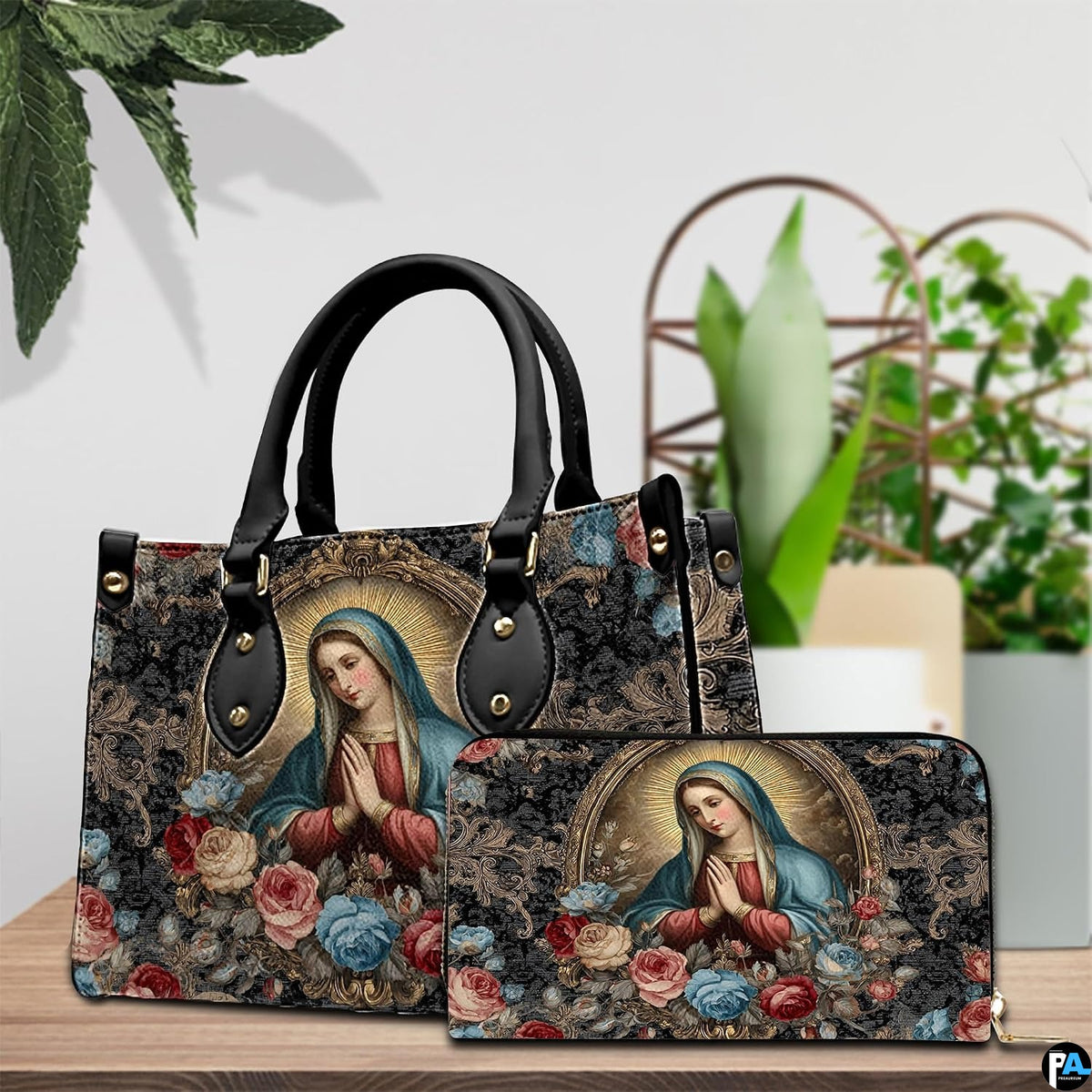 Tabletop lifestyle display showing baroque Madonna handbag and matching wallet beside potted house greenery.