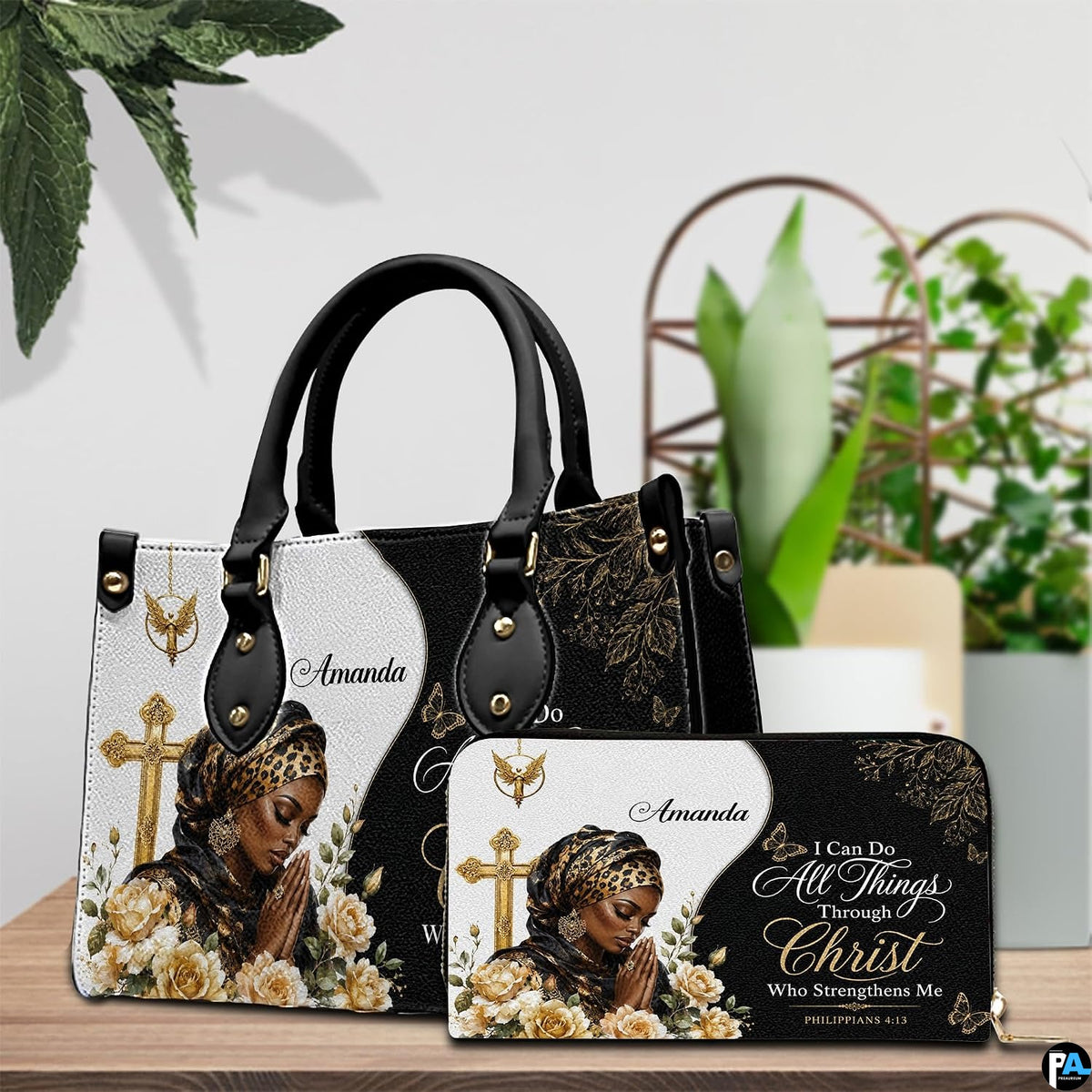 Praying woman handbag and coordinating wallet set arranged on a wooden table near green plants