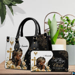 Praying woman handbag and coordinating wallet set arranged on a wooden table near green plants