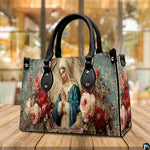 Lifestyle display showing handheld carry of the floral Virgin Mary handbag outdoors.