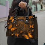 Outdoor street perspective of a model holding the bronze butterfly handbag by its top handles.