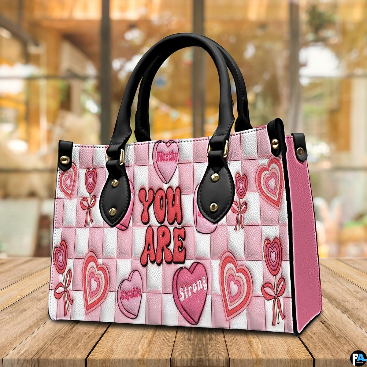 Perspective view of pink affirmation handbag resting on a wooden tabletop.