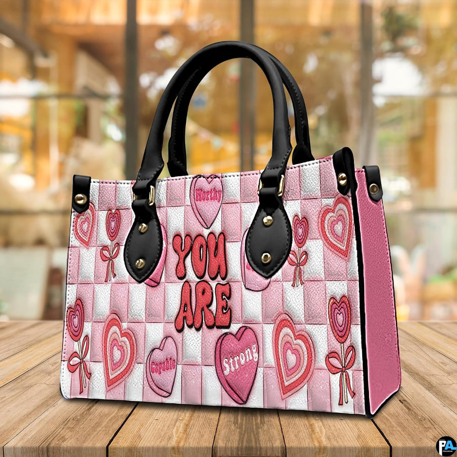 Perspective view of pink affirmation handbag resting on a wooden tabletop.