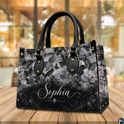 Gothic skull handbag and wallet displayed on wooden table beside potted plant.