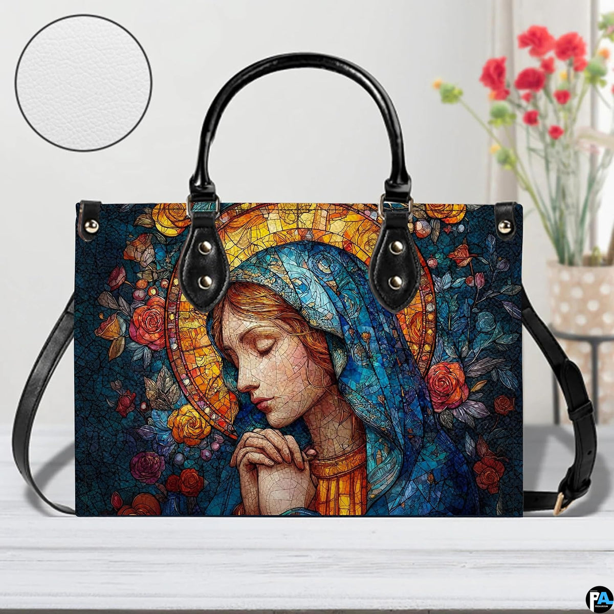 Praying Madonna handbag displayed on white surface beside floral decor.