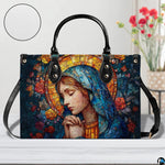 Praying Madonna handbag displayed on white surface beside floral decor.