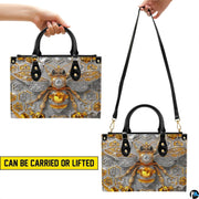 Side profile of bee handbag showing structured silhouette and black carrying handles.