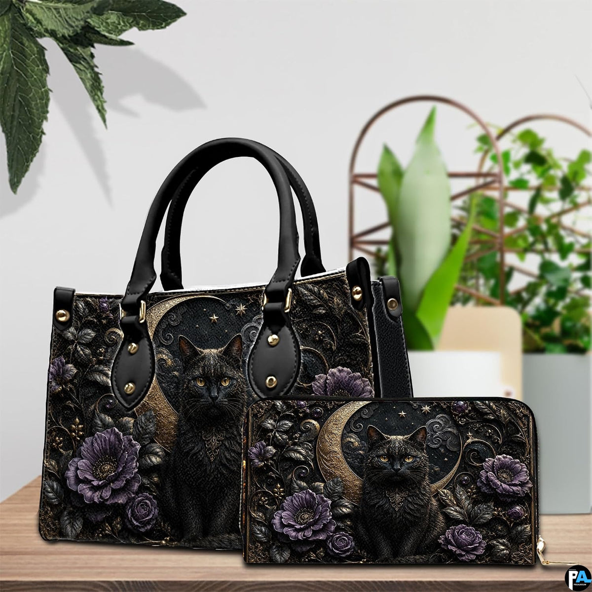 Tabletop view of gothic black cat and moon artwork placed beside indoor house plants on wooden table.