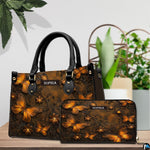 Golden butterfly handbag and matching wallet resting together on a wooden tabletop near potted greenery.
