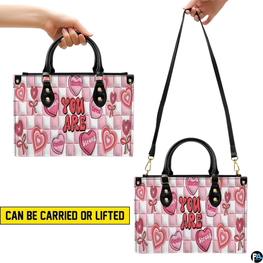 Dual display showing handheld carrying and shoulder wear for pink affirmation handbag.