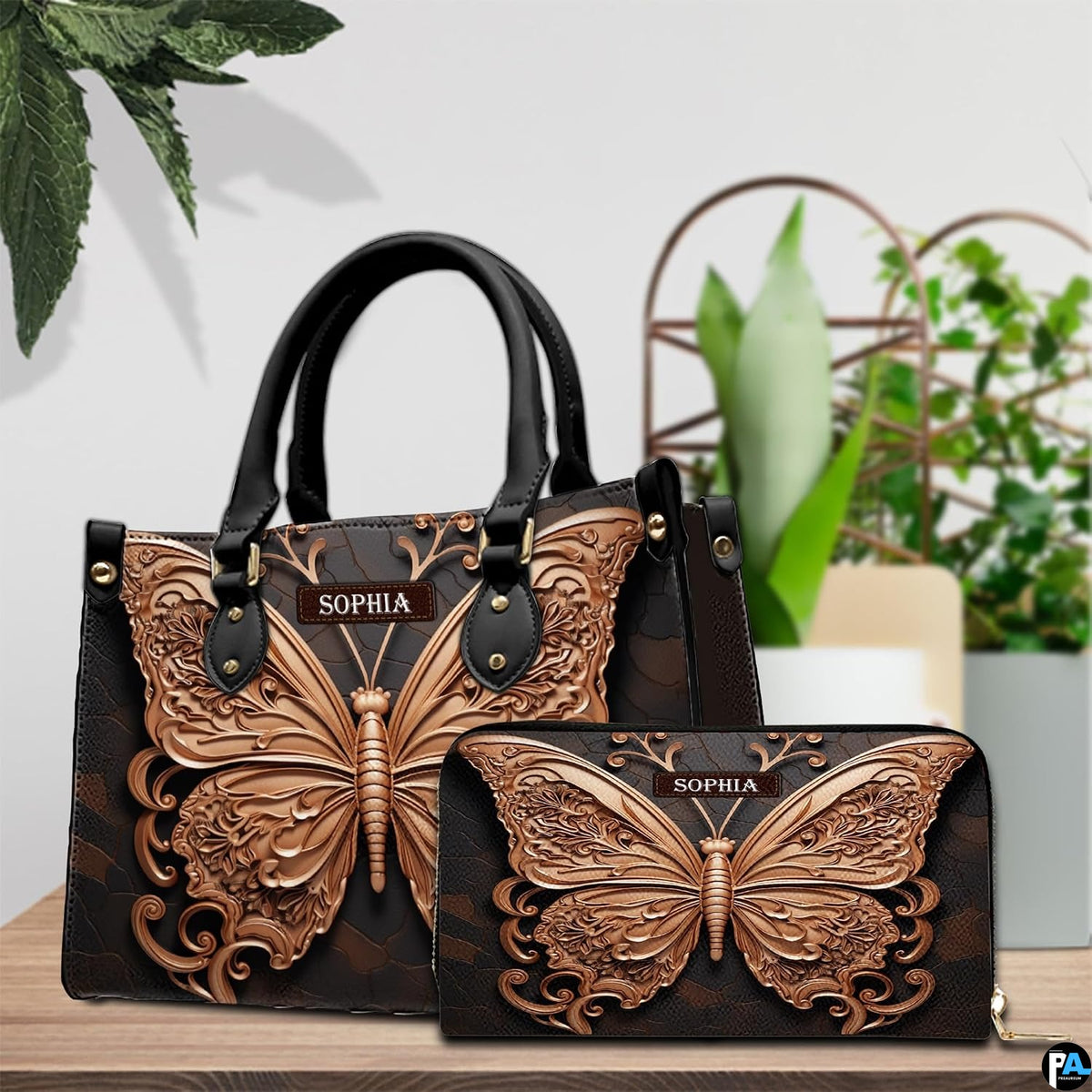 Sculpted rose gold butterfly handbag and matching wallet resting together on a wooden table near green plants.