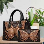 Sculpted rose gold butterfly handbag and matching wallet resting together on a wooden table near green plants.