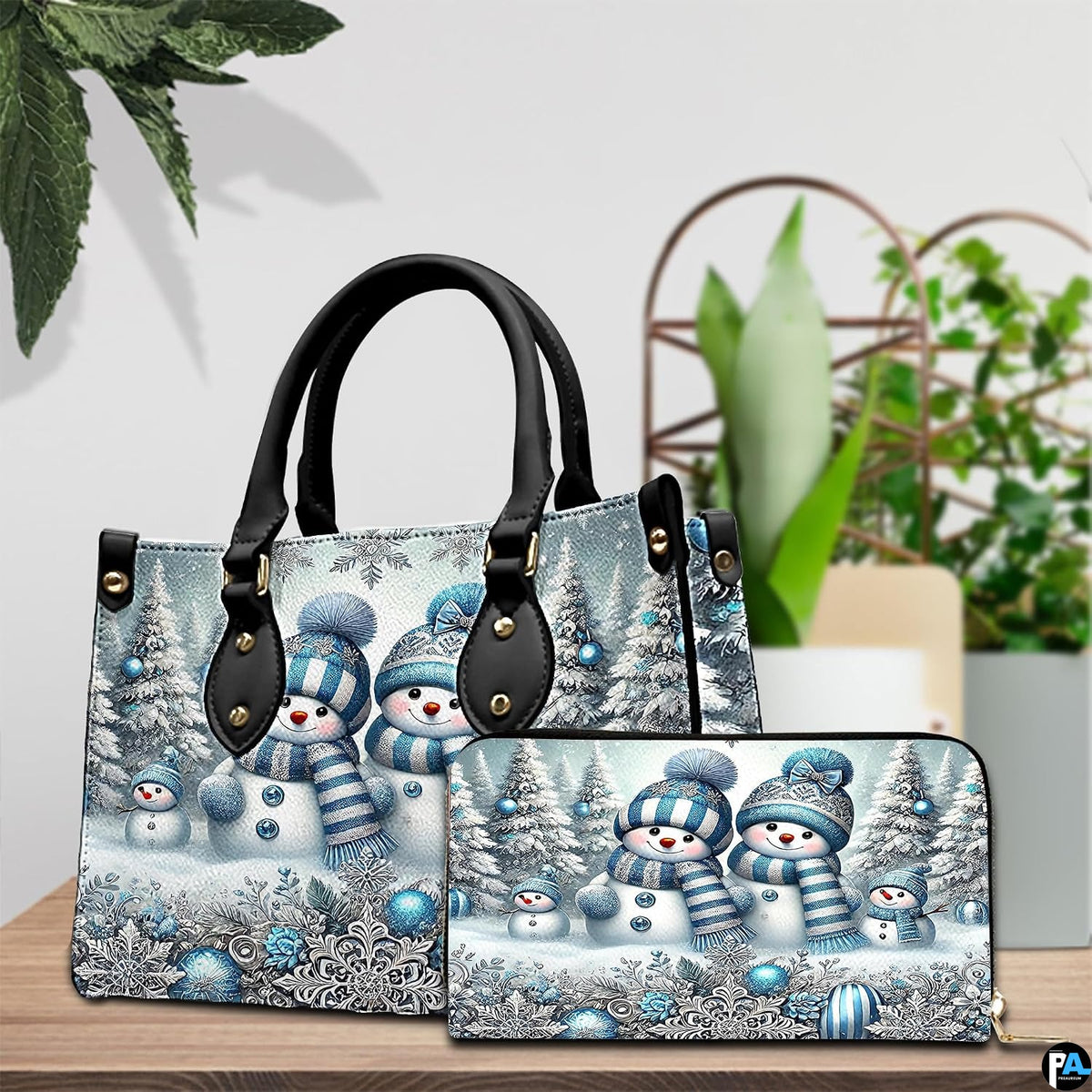 Coordinated blue snowman family duo displayed on a wooden tabletop beside green foliage.