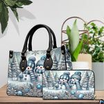 Coordinated blue snowman family duo displayed on a wooden tabletop beside green foliage.