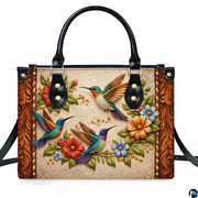 Front studio shot of handbag showcasing three colorful hummingbirds and embossed scrollwork motif.