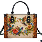 Front studio shot of handbag showcasing three colorful hummingbirds and embossed scrollwork motif.