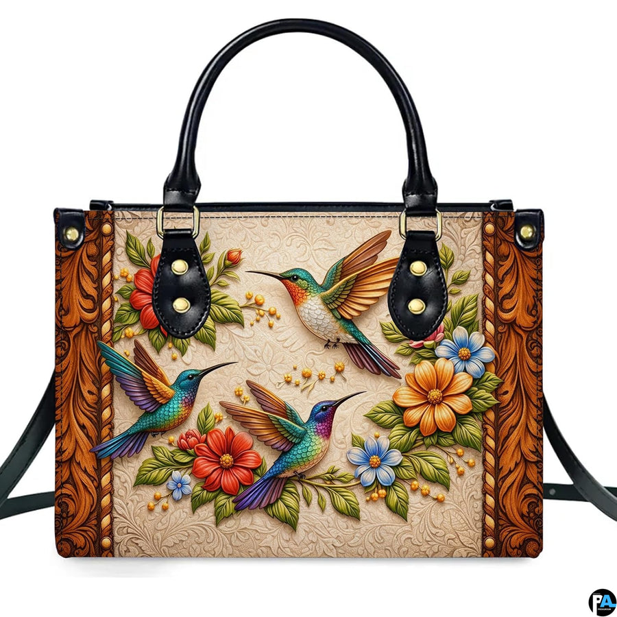 Front studio shot of handbag showcasing three colorful hummingbirds and embossed scrollwork motif.