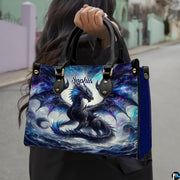 Cosmic dragon handbag carried outdoors by top handles displaying the vibrant cyan and purple dragon artwork.