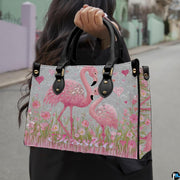 Side angle view of pink flamingo handbag with floral meadow illustrations and silver backdrop.