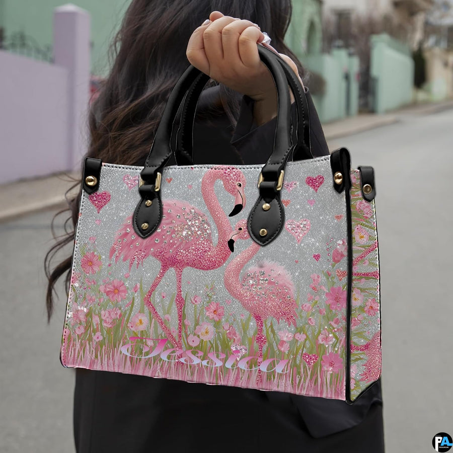 Side angle view of pink flamingo handbag with floral meadow illustrations and silver backdrop.