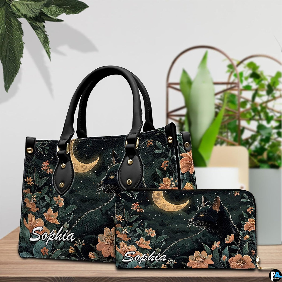 Celestial cat and moon botanical artwork displayed on a wooden surface beside house plants.