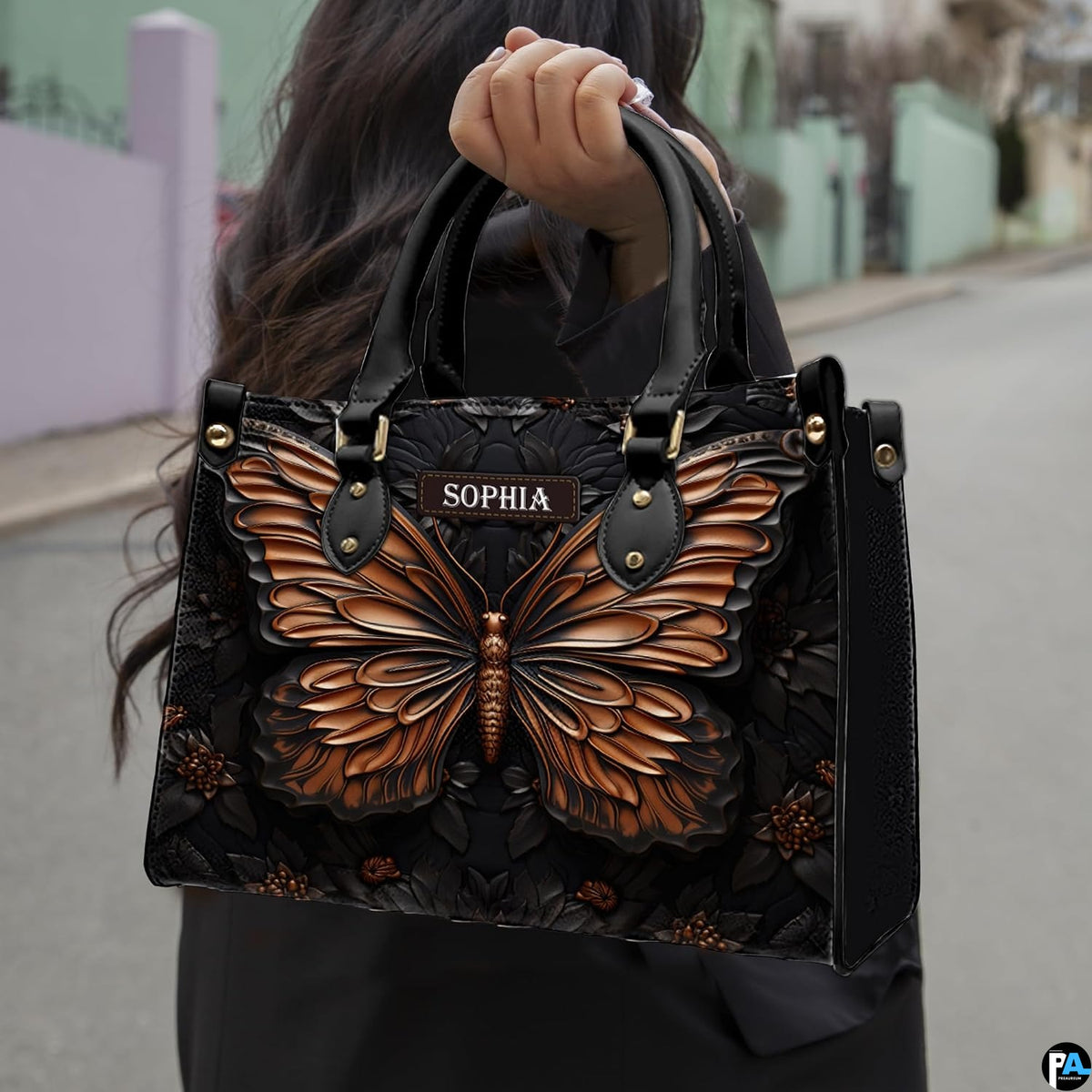 Outdoor street view of a model carrying the black and copper butterfly handbag by its top handles.