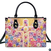 Frontal view of handbag featuring a glowing pastel floral cross with golden sunburst rays on floral field.