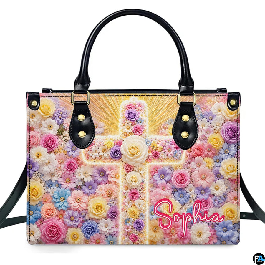 Frontal view of handbag featuring a glowing pastel floral cross with golden sunburst rays on floral field.