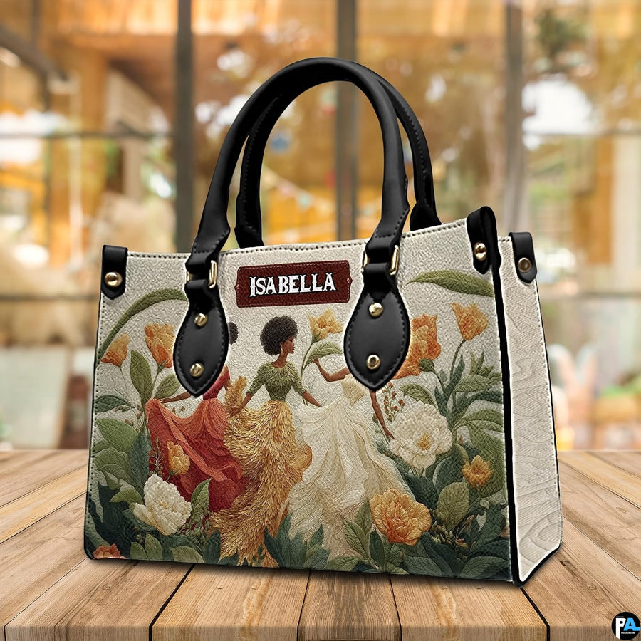Angled cafe view of the structured floral artwork handbag resting on a polished wooden surface.