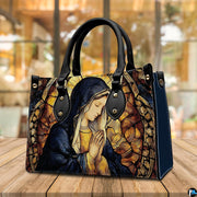 Praying Madonna cathedral art handbag resting on an outdoor wooden table surface