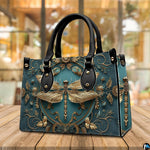 Angled perspective view of gold dragonfly handbag resting on a rustic wooden tabletop near a window