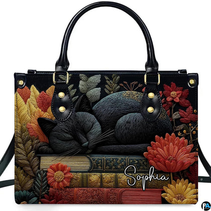 Studio display of Sleeping Black Cat Library Books Handbag showing sleeping feline on stacked books with autumn flowers.