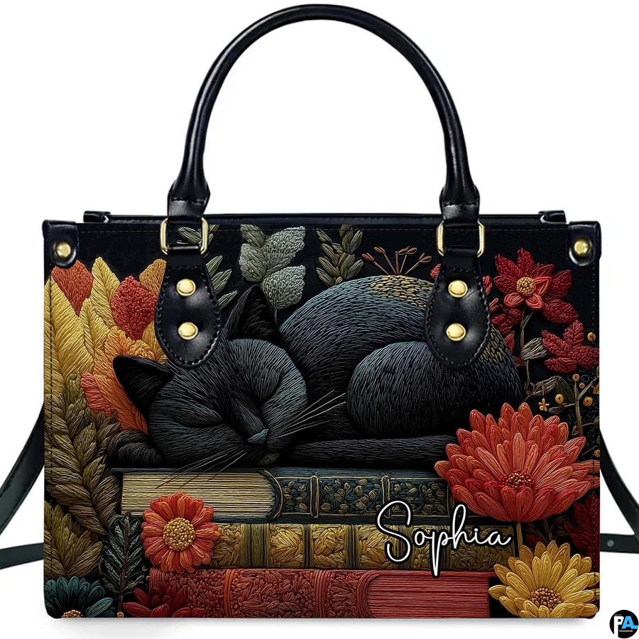 Studio display of Sleeping Black Cat Library Books Handbag showing sleeping feline on stacked books with autumn flowers.