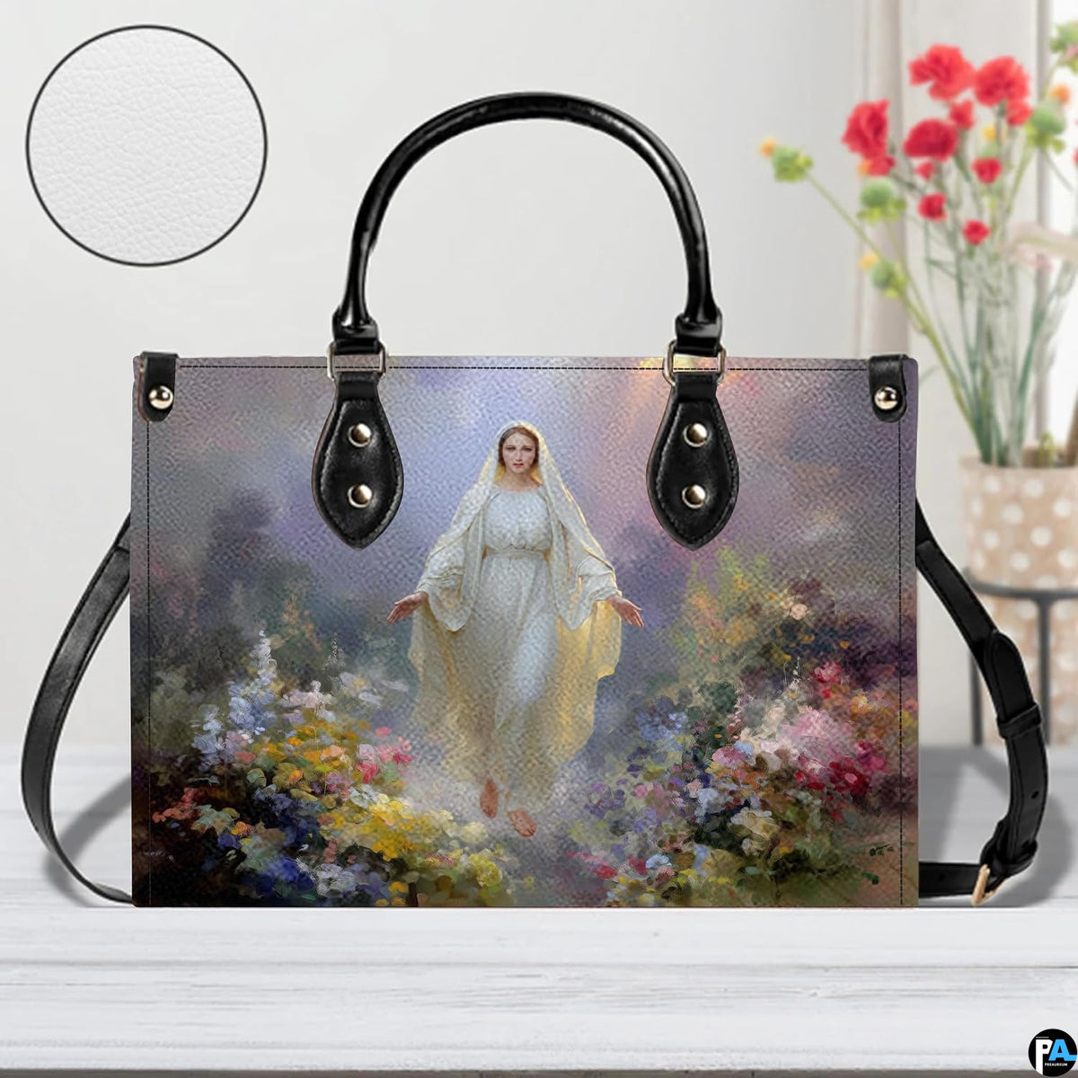 Lifestyle tabletop view of Our Lady of Grace floral handbag beside white texture swatch.