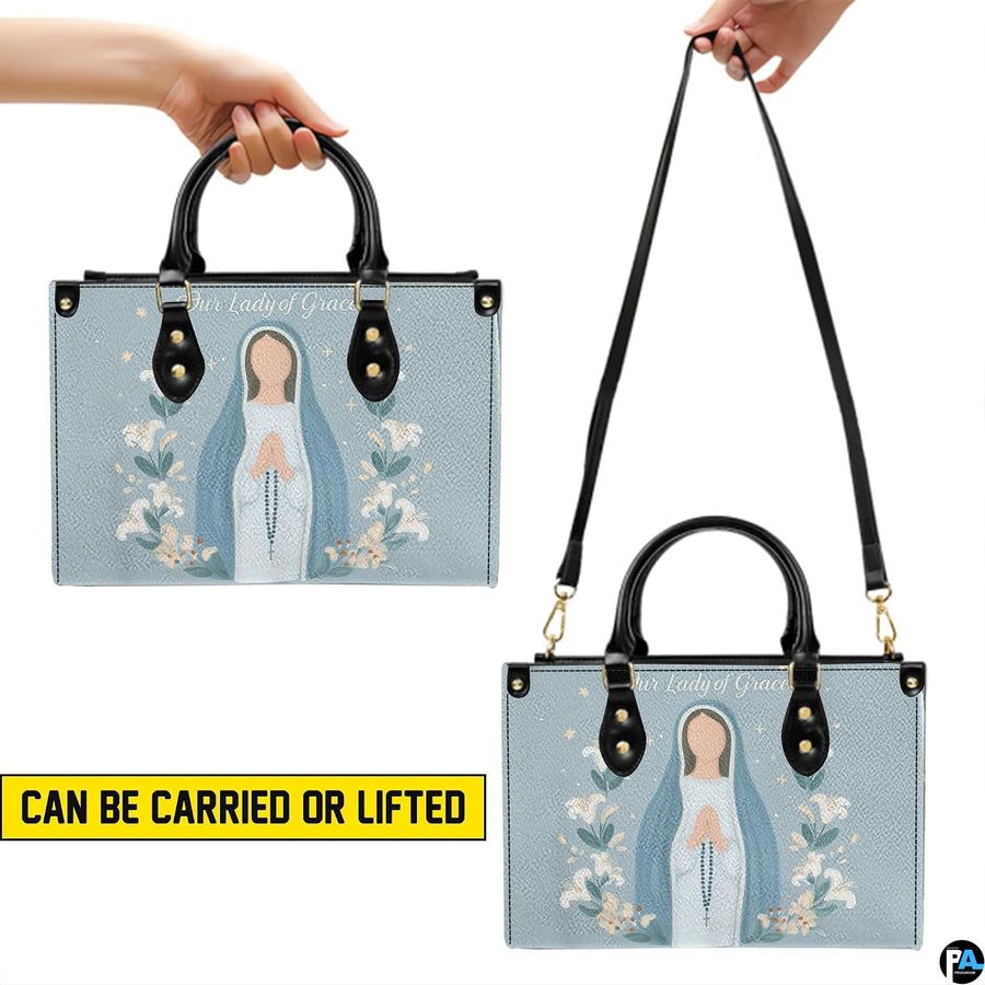 Pastel blue Virgin Mary lily handbag shown held by top handles and shoulder strap