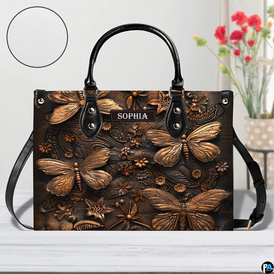 Artisan dragonfly handbag displayed on a white surface alongside floral decor and a circular material swatch.