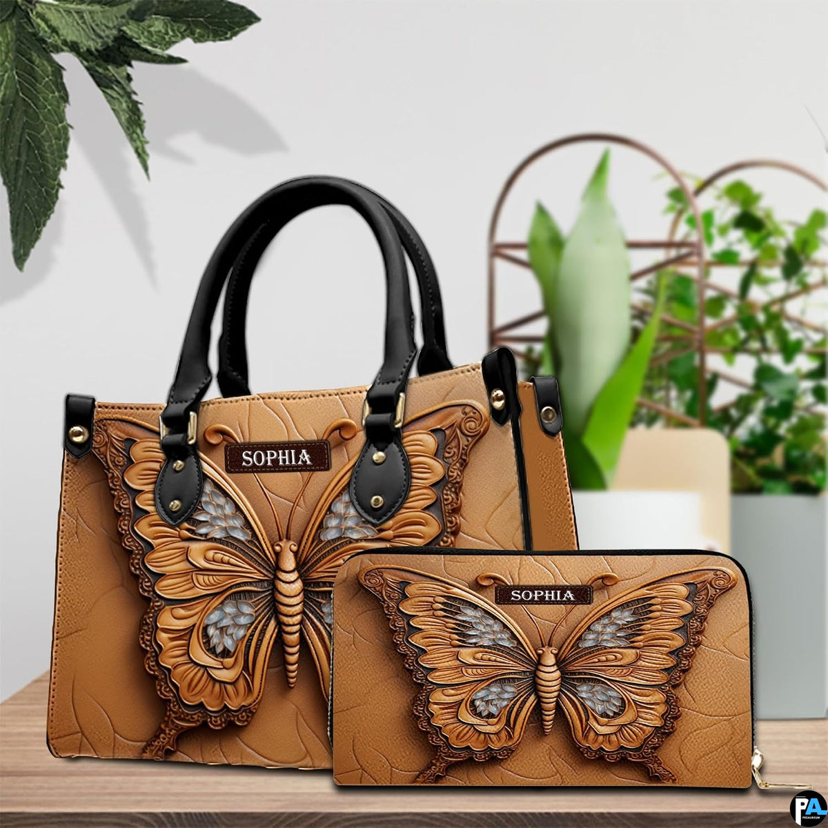 Embossed caramel butterfly handbag and matching wallet resting together on a wooden table beside houseplants.