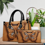 Embossed caramel butterfly handbag and matching wallet resting together on a wooden table beside houseplants.