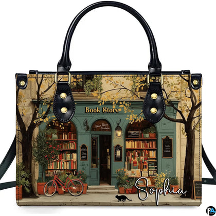 Studio display of Teal Bookshop Facade Handbag showing arched storefront, vintage red bicycle, and black cat.