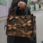Outdoor street view of a model carrying the bronze dragonfly handbag by its top handles.