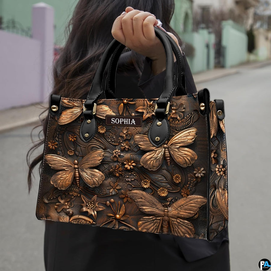 Outdoor street view of a model carrying the bronze dragonfly handbag by its top handles.